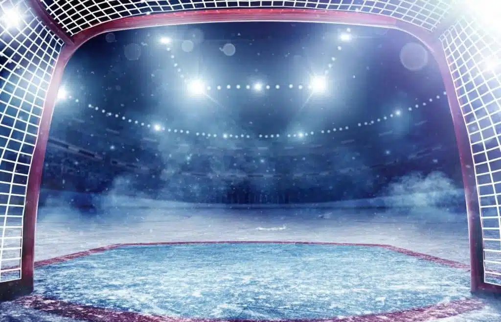View of the ice rink from inside of the ice hockey goal with the ice adding a misty haze and bright lights  enhancing the anticipation.