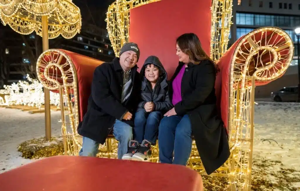 Mother, father and son posing for the camera while stiing on a giant red chair decorated with festival lights