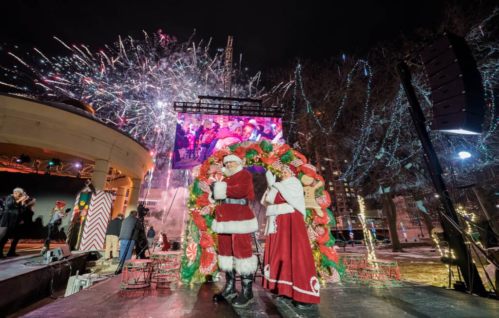 Mrs and Santa Clause standing in front of a giant Christmas wreath during the Milwaukee Holiday Lights Festival Kickoff