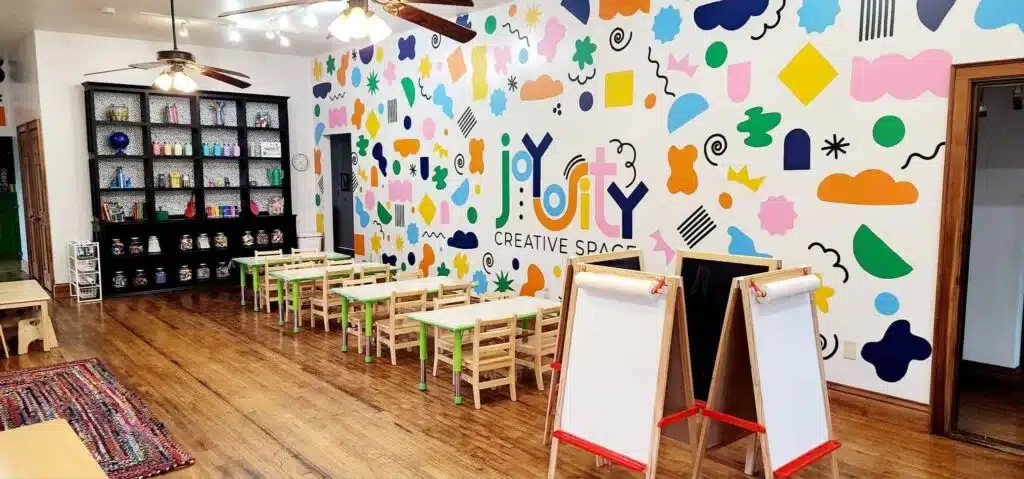Joyosity Creative Space classroom with colorful mural, craft tables, and easels ready for kids.