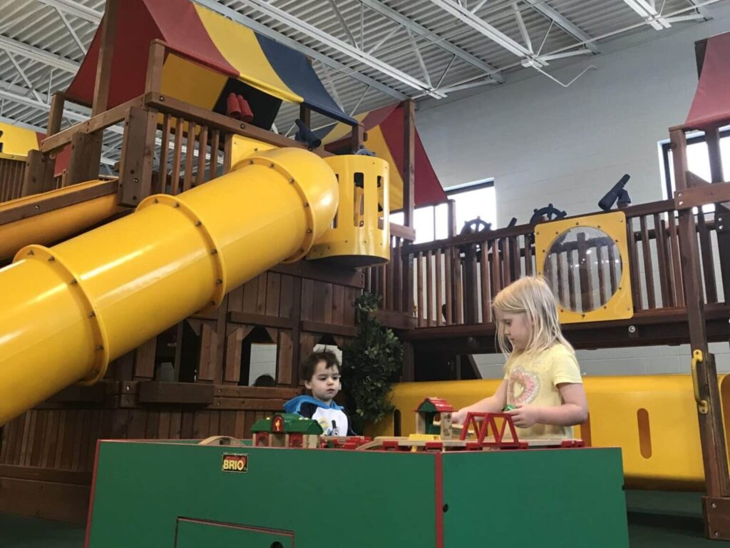 Two kids playing toys beside a large tunnel slide with a walking bridge made of wood at Just 4 Fun Playland