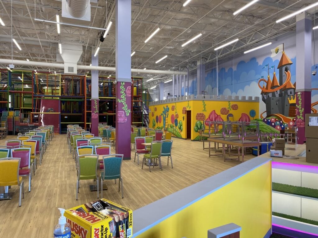 A playful castle mural, play structures and play areas with a large space with colorful tables and chairs at Kids Empire.