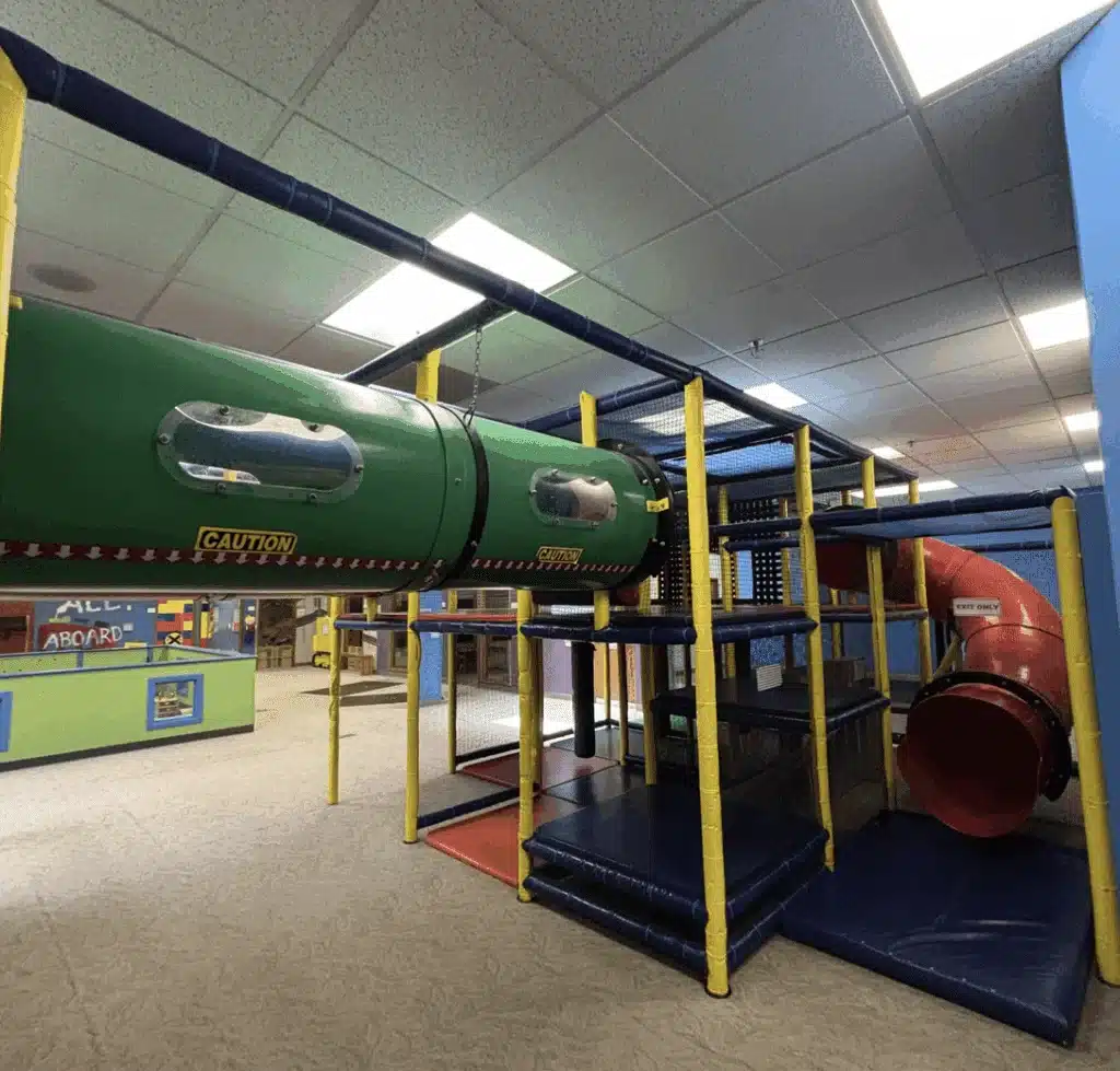 A play gym with a red tunnel slide and planks at Kids in Motion