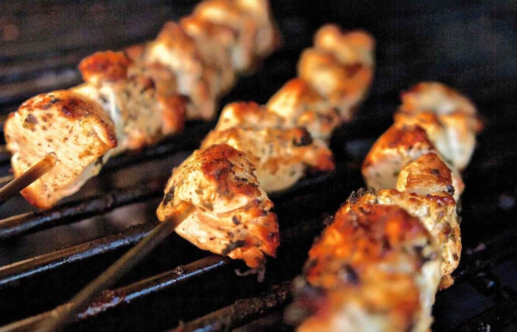 Chicken on skewers still being roasted on grill
