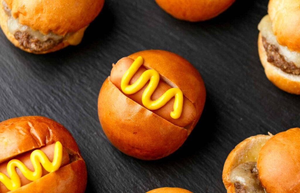 Small buns with mini hotdogs topped with mustard