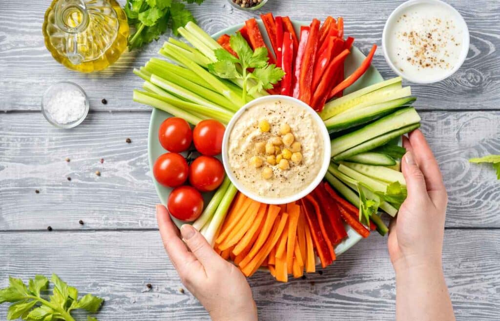 A plate full of slices of celery, bell pepper, carrots and cucumber and tomatoes served with dip