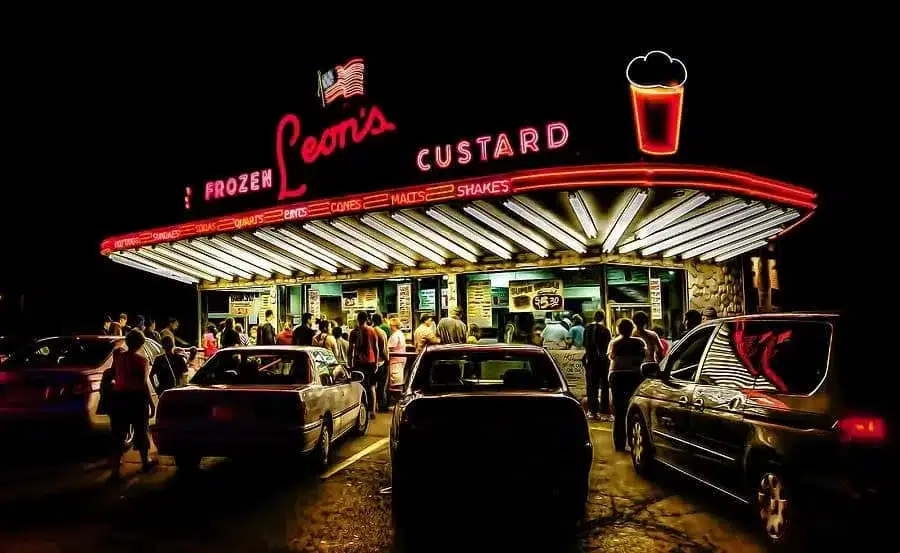 Nighttime view of Leon’s Frozen Custard stand glowing with neon lights and customers.