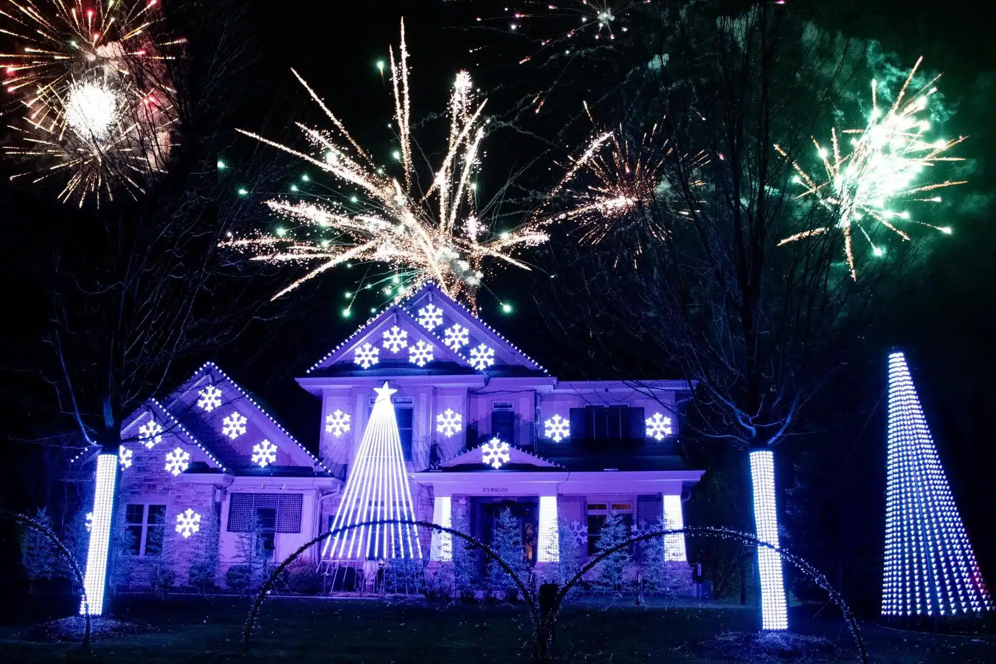 A home decorated with light display featuring snowflakes and stars with fireworks in the sky
