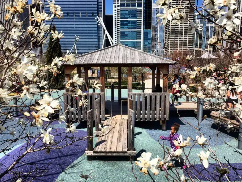 Kids playing in the Maggie Daley Park Play Garden, surrounded by blooming spring trees and colorful playground structures.