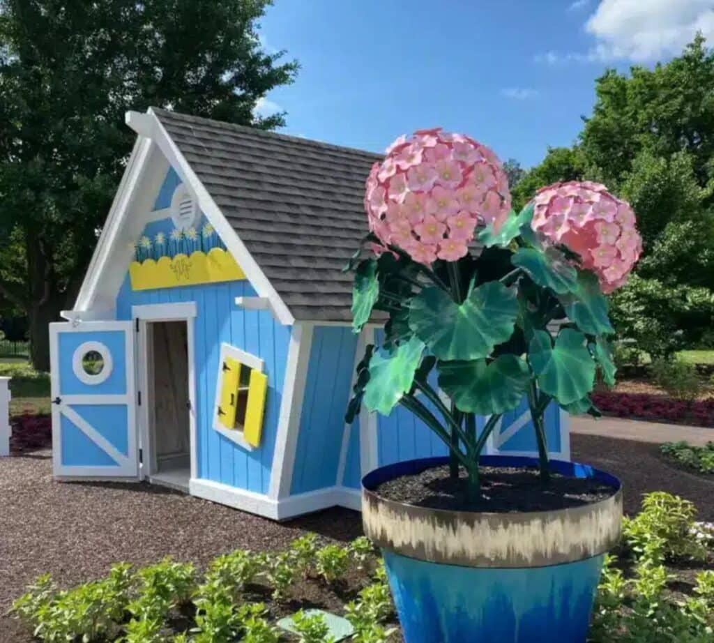 Blue potter's shed and large pink flower sculpture at Margie's Children's Garden.