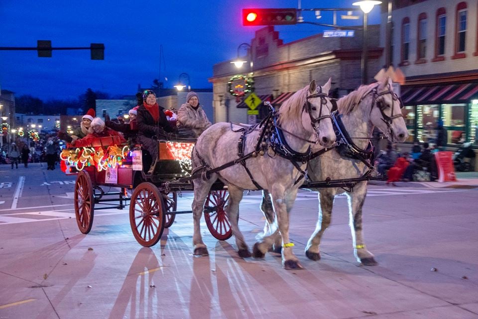 A red open carriage and drawn by two white horses with people waving to the onlookers during the Menomonee Falls Christmas Parade. 