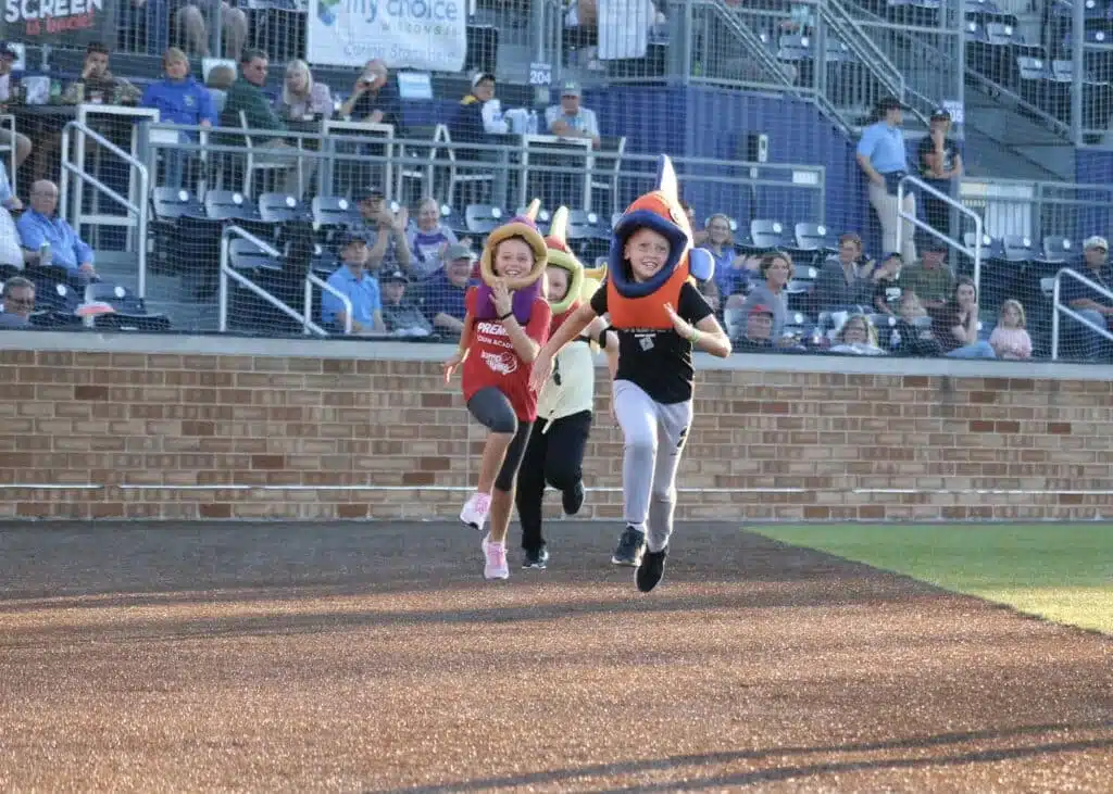Kids dressed as fish race on the field during a fun promotion.