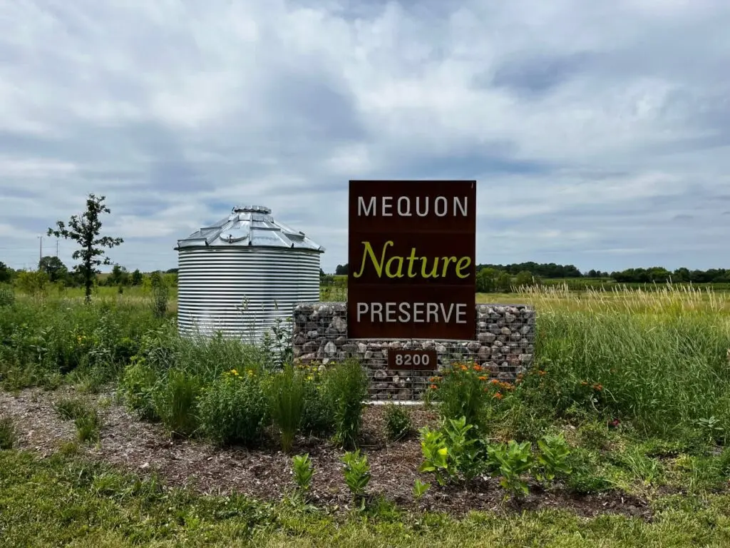 A sign that says Mequon Nature Reserve and beside it is a large water tank