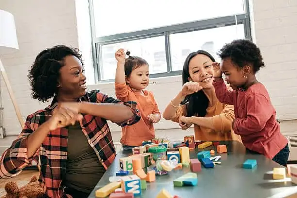 Caregivers and toddlers playing with blocks and toys indoors.