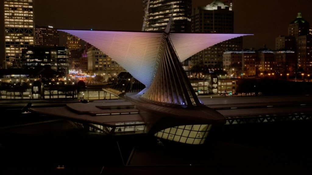 The Burke Brise Soleil illuminated in soft pastel colors, with the Milwaukee skyline shining brightly in the background