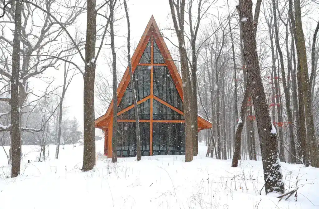 Conservancy for Healing & Heritage A-frame healing chapel covered in snow, surrounded by trees during snowfall.
