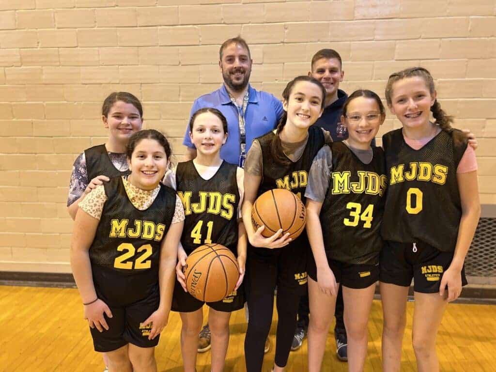 A girl's basketball team consisting of 6 players with the MJDS basketball uniform with their two coaches