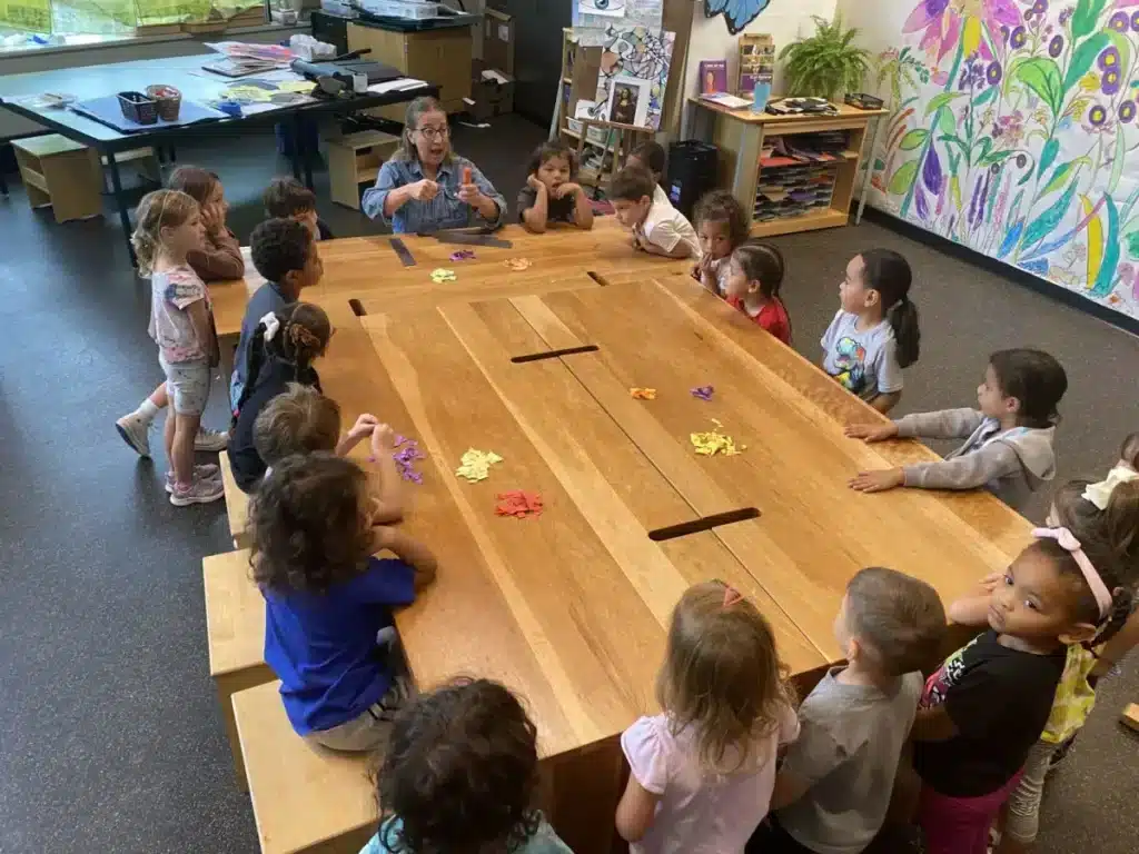 A teacher talking to kindergarten students who are sitting around a rectangular table