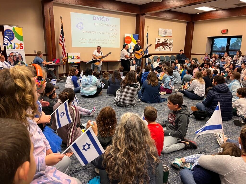 People sitting on the floor and holding the Israel flag while listening to people singing