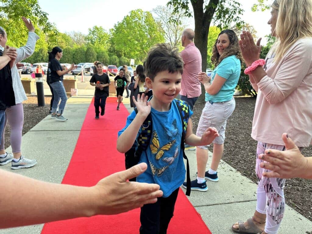 Parents clapping while kids are walking on a red carpet while a boy is about to do a high-five