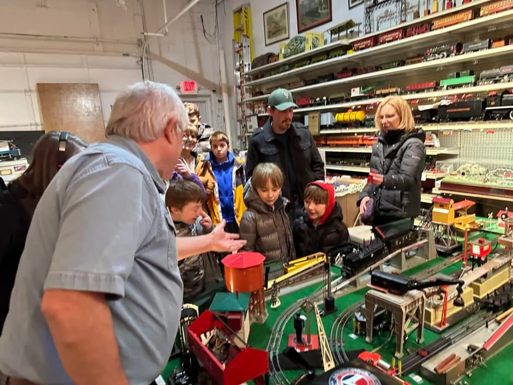A man talking about trains and railroads while young kids are looking at model trains