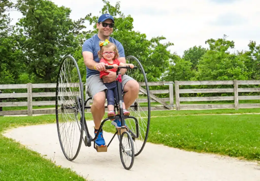 Father and daughter riding an old-style bicycle with large wheels