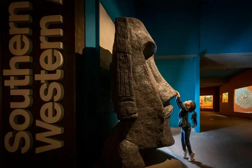 A little girl touching the nose of the moai exhibit at the Milwaukee Public Museum