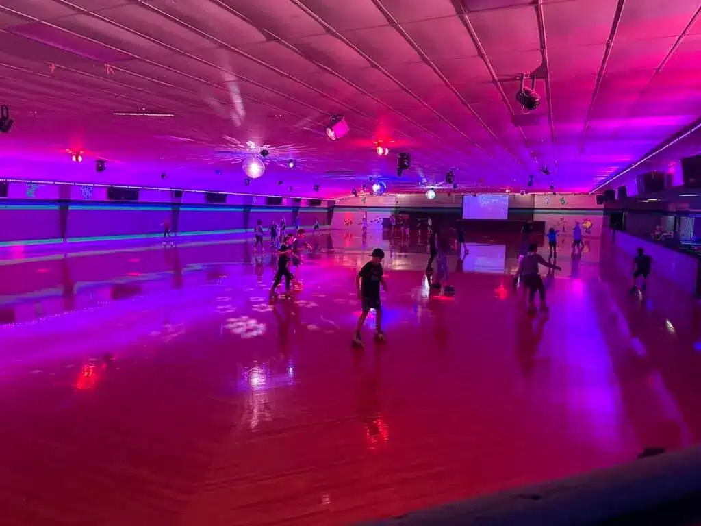 People having having in a roller skating rink with pink lights and large TV in Milwaukee