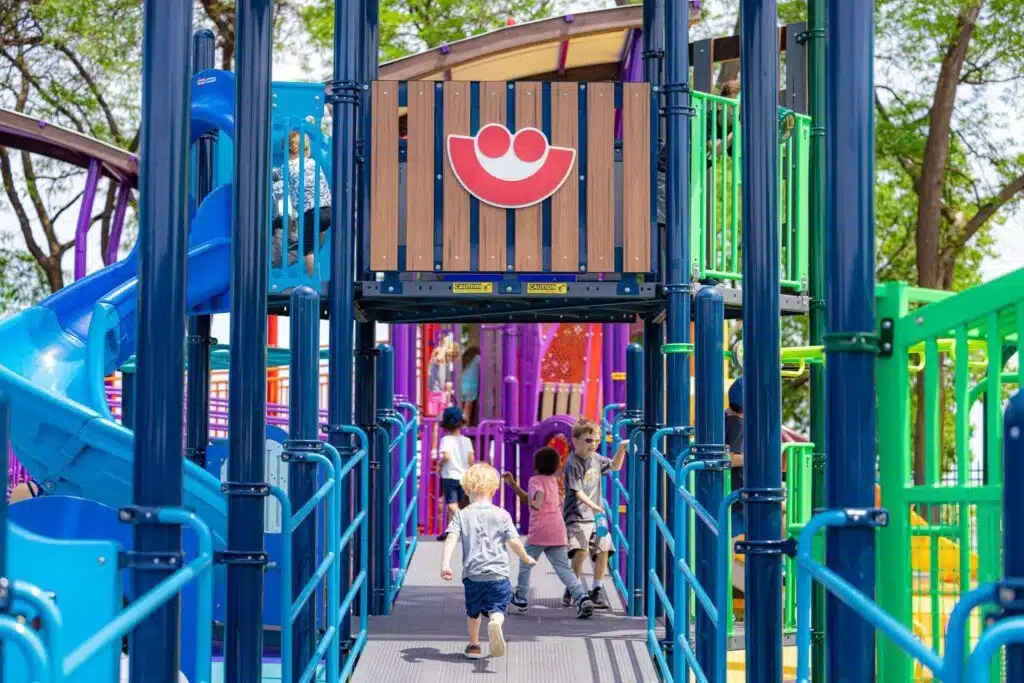 Kids playing at a community playground with the Summerfest smile logo placed on wood panel