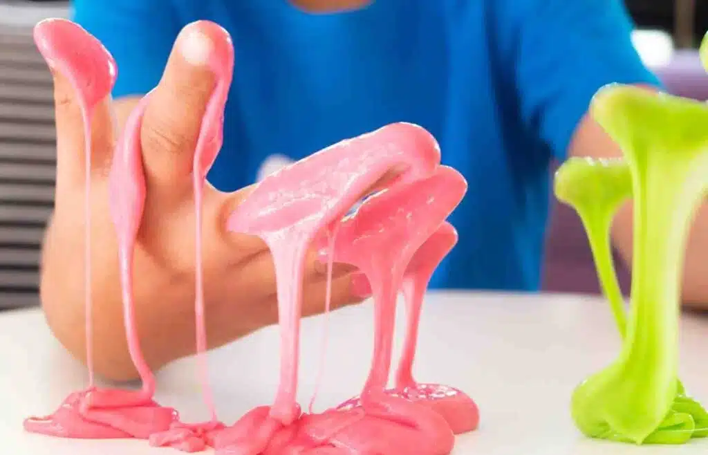 Child stretching green and pink slime during a hands-on winter science activity indoors.