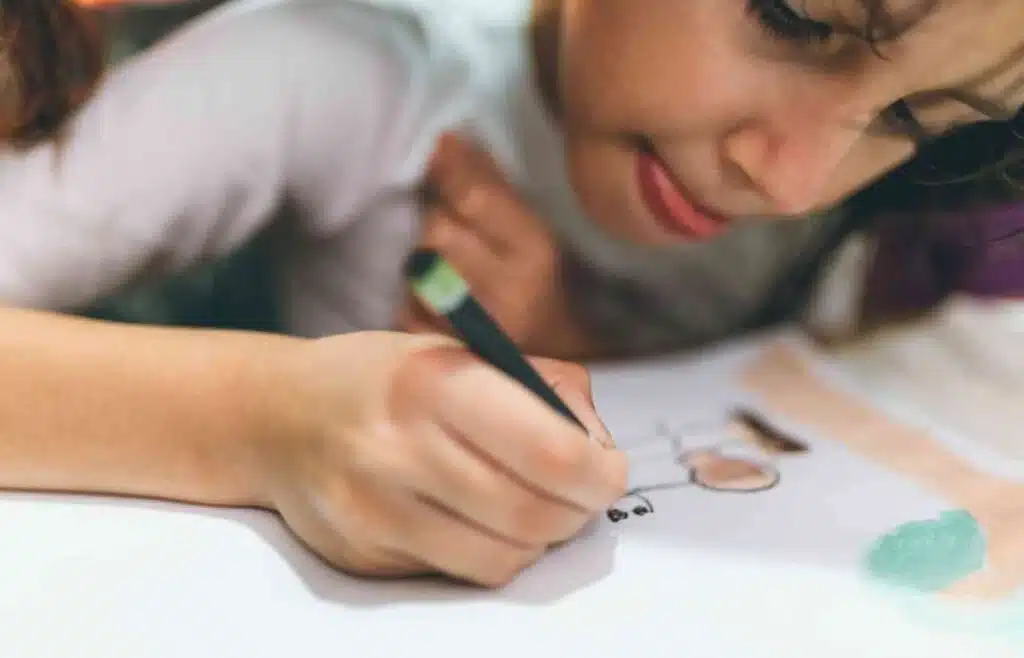 Child concentrating while drawing a colorful picture with crayons.