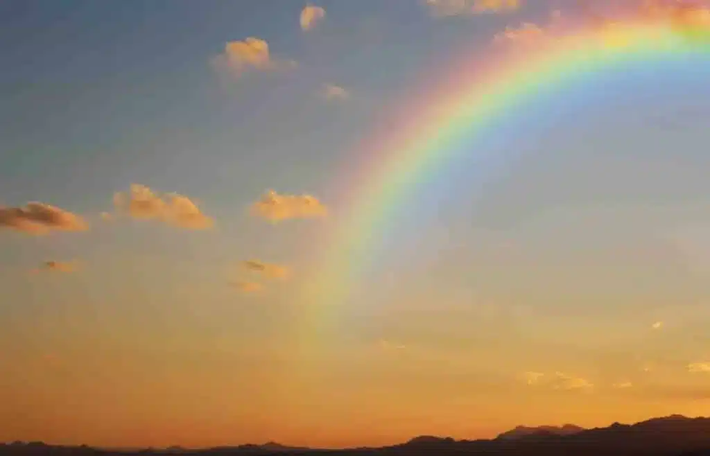 Bright rainbow arching across the sky after a rainstorm at sunset.