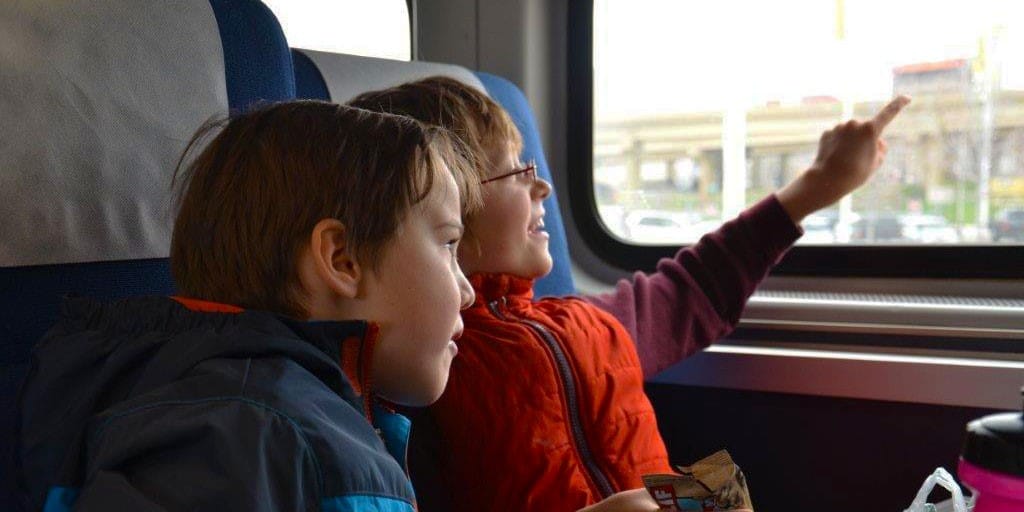 Two children sitting by the window on an Amtrak train, watching the view and pointing outside.