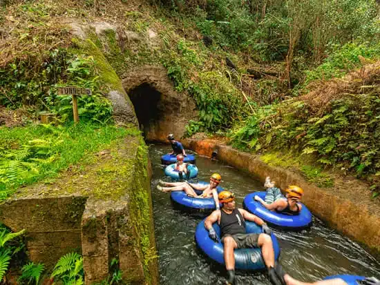Five people with headlamps riding blue inner tubes in an irrigation tunnel in Kauai