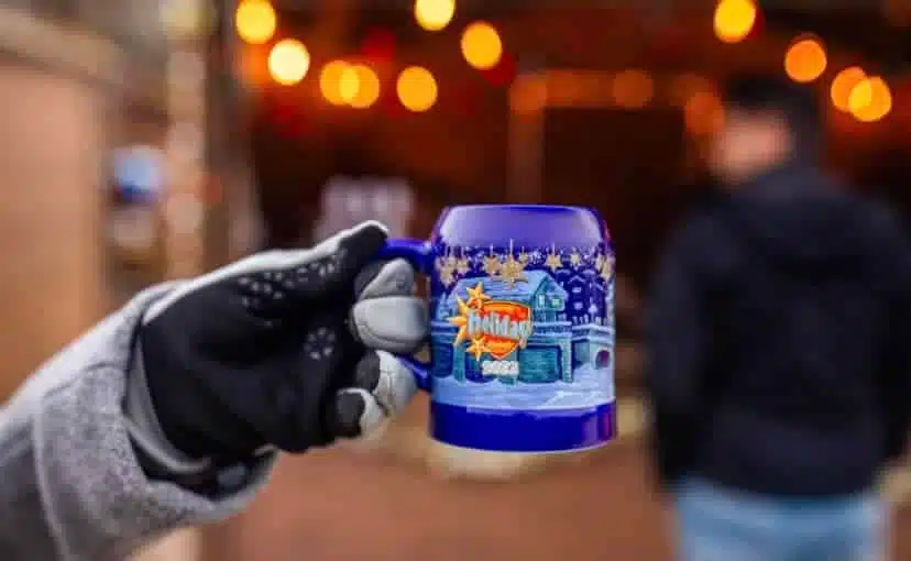 Gloved hand holding a blue Christmas mug at a holiday market