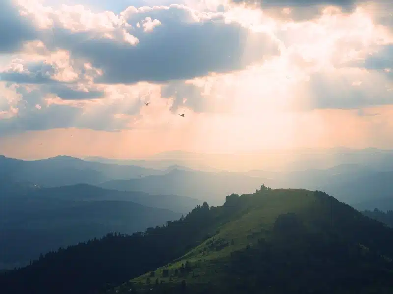Soft morning light streaming through clouds over a quiet hilltop.