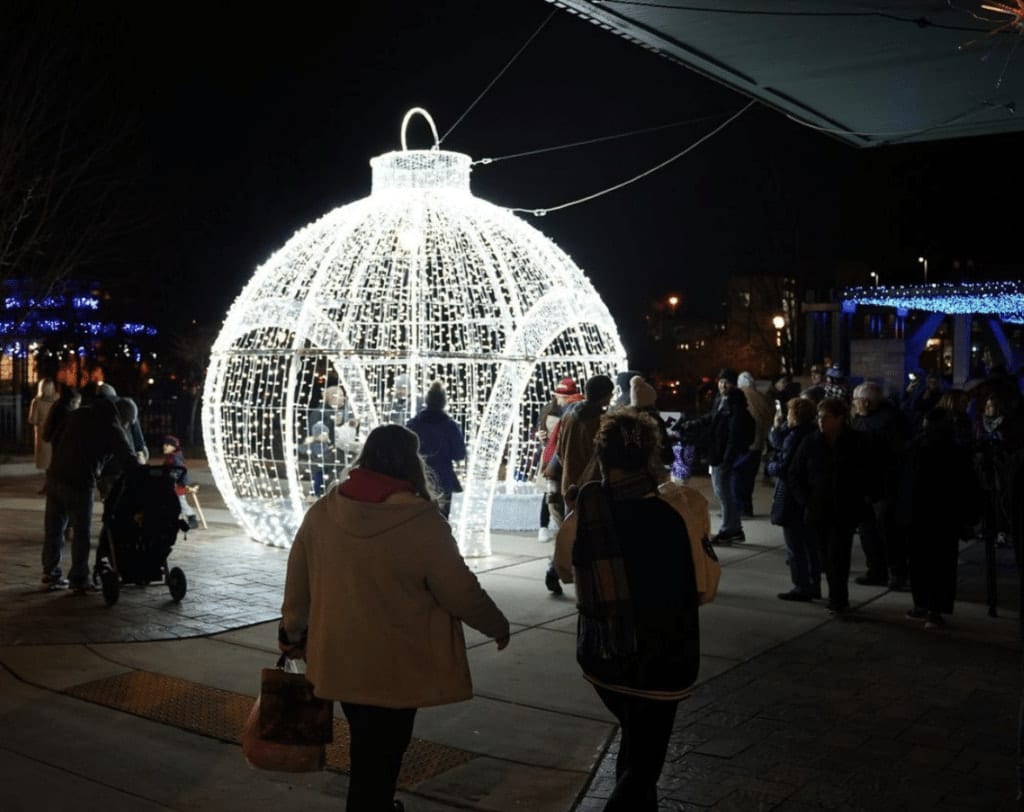 People passing a large Christmas ball decorated with lights during the Waukesha Nights of Lights event.