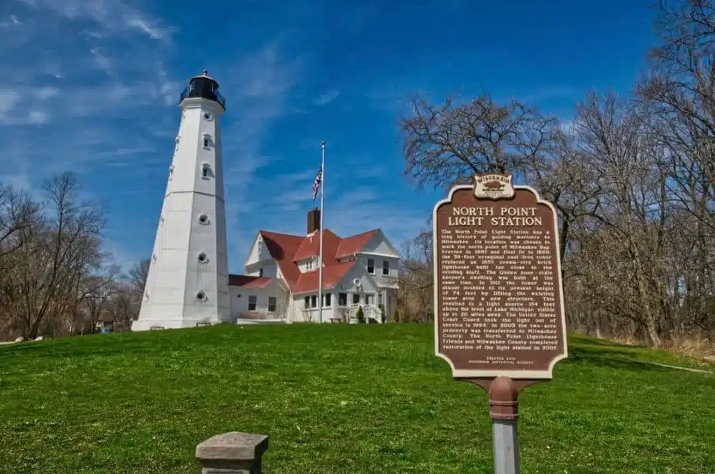 A brown historical marker of the North Point Light Station and Museum in Milwaukee with the American flag in the background