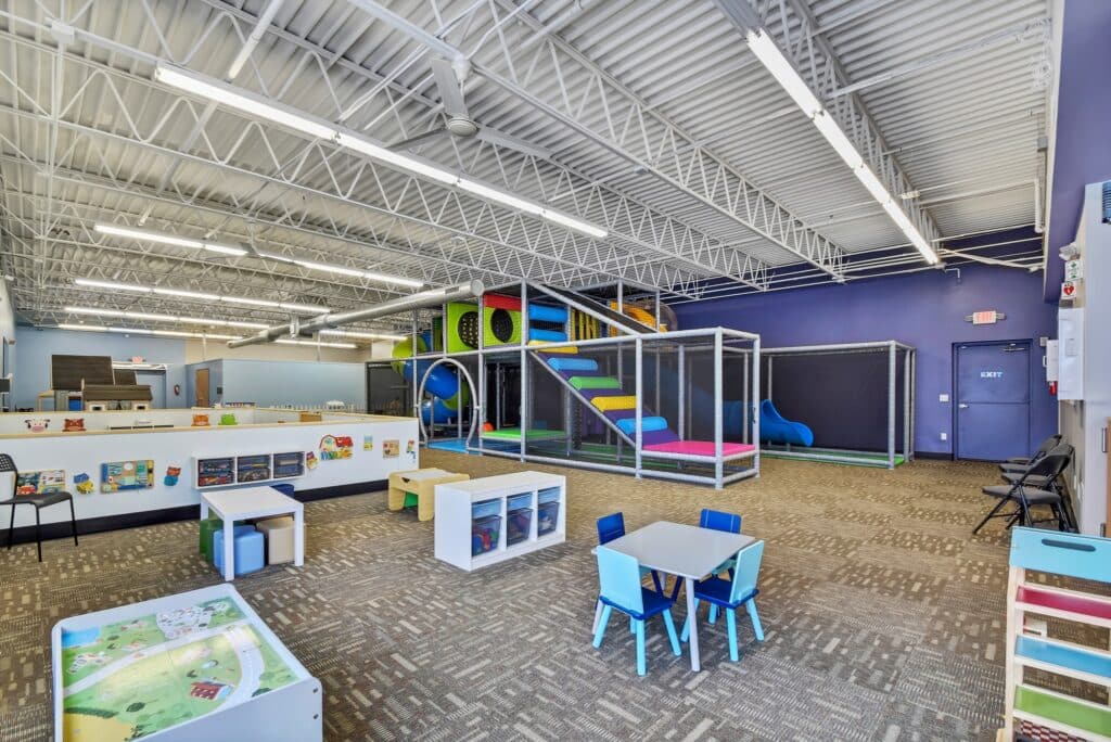 Modern indoor play area with slides, low-sitting tables and chairs, high ceiling and bookshelves at Nugget Nation MKE