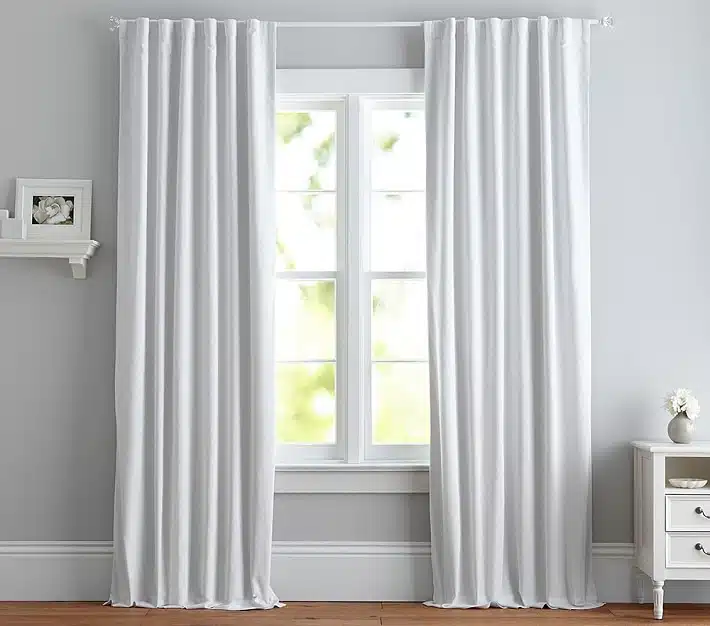 White Pottery Barn Kids blackout curtains covering a nursery window for a cleaner, darker sleep space.