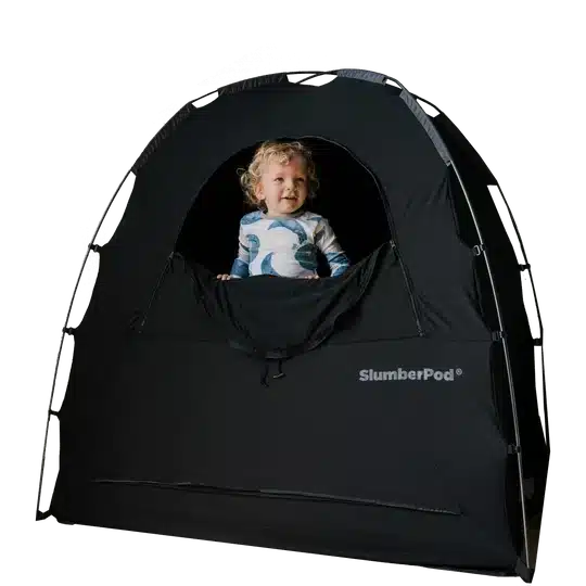 Toddler sitting inside a black SlumberPod sleep tent designed to create a dark travel sleep space.