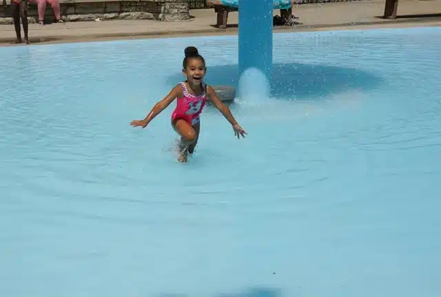 A little girl in pink suit and hair bun  happily playing at the Ohio Playfeild wading area