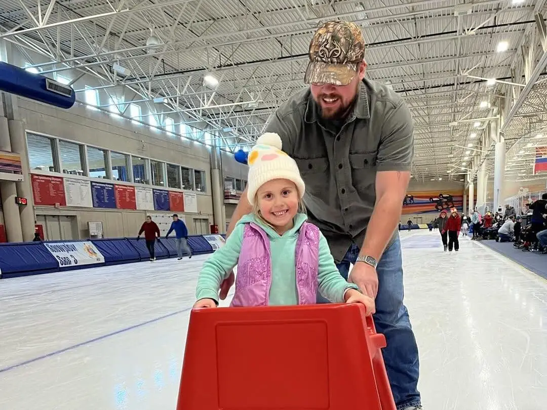 Child learning to ice skate using a red skate aid at Pettit National Ice Center