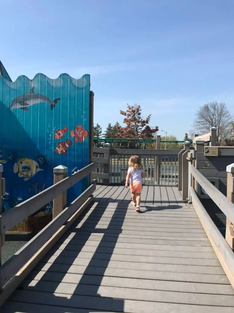 A young child walks up the ramp at Possibility Playground in Port Washington, Wisconsin, with an ocean-themed climbing wall