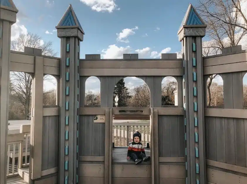 Child sitting inside wooden castle structure at Fort Cushing Playground in Delafield.