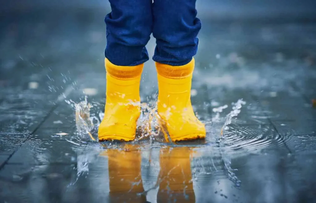 Child wearing yellow rain boots splashing in a puddle.