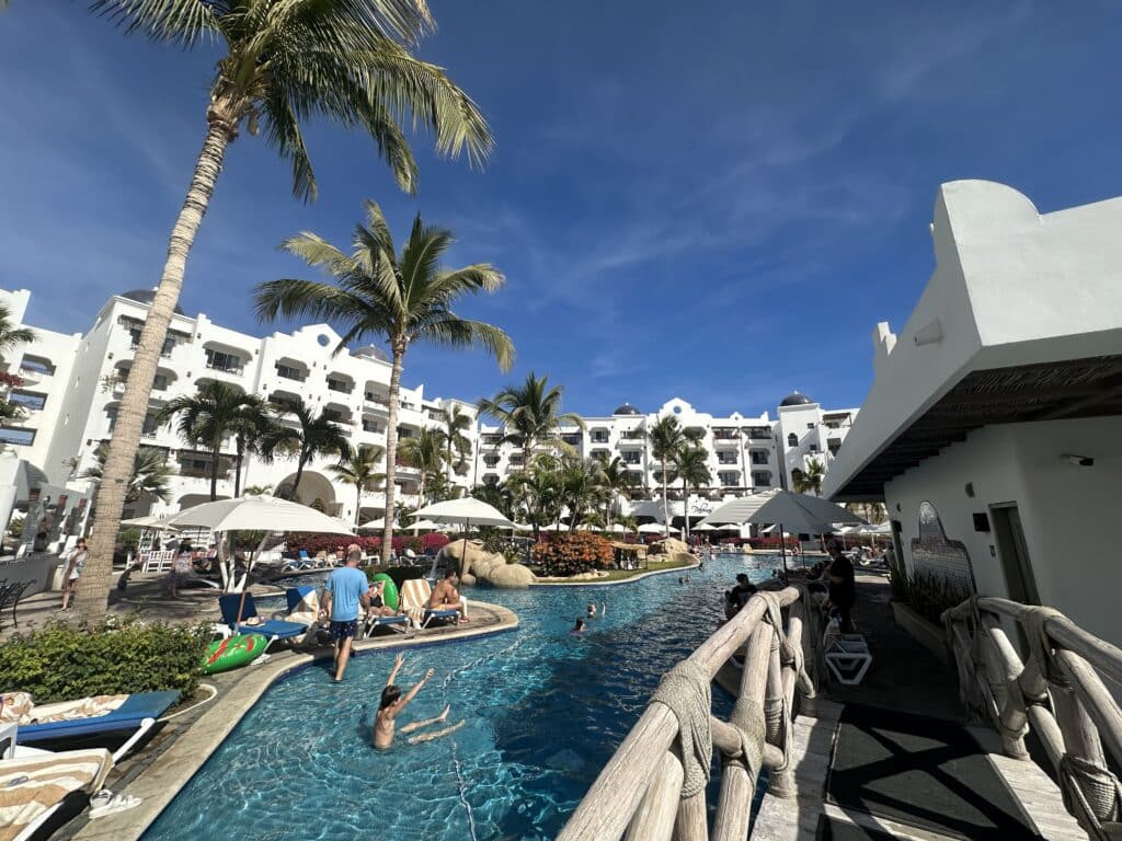 A serene view of the Pueblo Bonito Los Cabos resort pool surrounded by palm trees, with bright blue skies in the background.