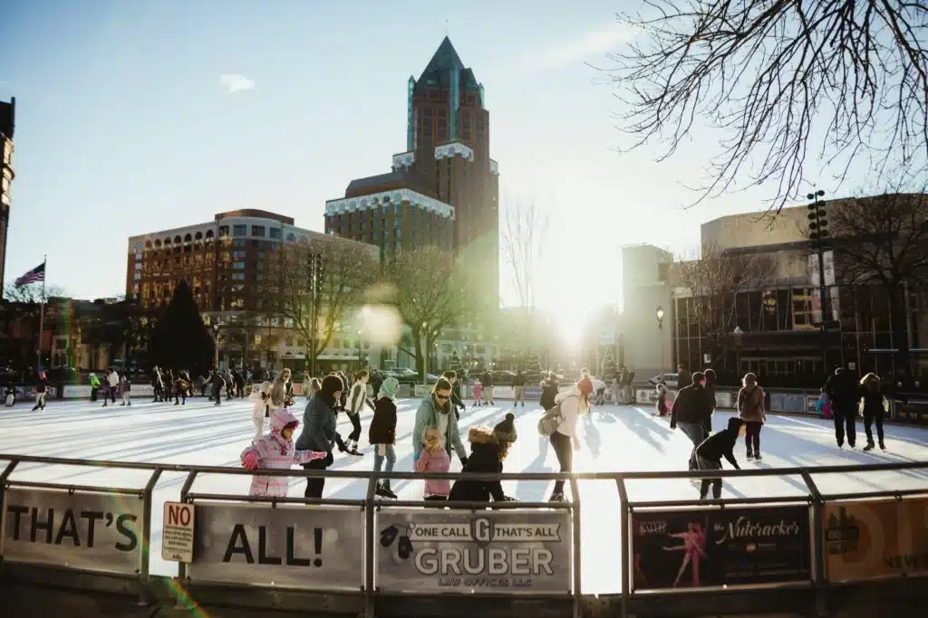 Families ice skating at Red Arrow Park in downtown Milwaukee during winter with city skyline in the background.