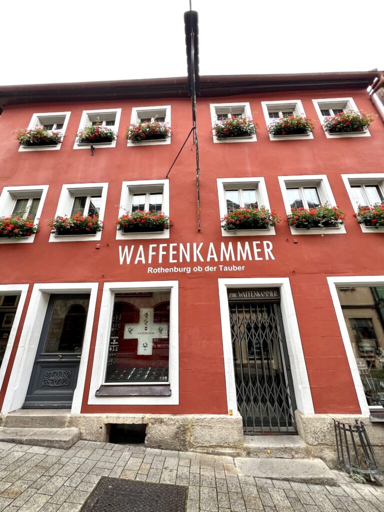 The red store front of Waffenkammer with white windows and grilled entrance door