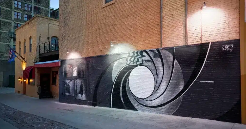Black-and-white spy-themed mural on exterior SafeHouse Milwaukee building at twilight.